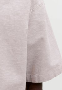 Gros plan sur la manche d'une chemise en coton rose clair à manches courtes avec des coutures visibles et une texture de tissu.