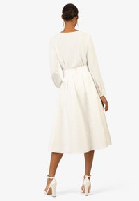 Robe blanche à manches longues avec un corsage ajusté et une jupe évasée, dotée d'une ceinture, d'une texture lisse et d'une fermeture éclair au dos.