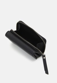 Portefeuille en cuir noir avec fermeture zippée, présentant un extérieur lisse et une languette de traction texturée. L'intérieur est non doublé et spacieux.