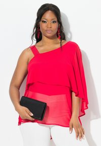 Top in chiffon rosso con design asimmetrico, spallina singola con borchie, silhouette a strati, abbinato a una borsa nera e pantaloni bianchi.