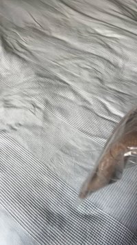 Šedá texturovaná látka s vodorovnými pruhy o různých šířkách; v rohu je viditelná část průhledného plastového sáčku.