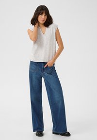 Haut sans manches gris clair avec décolleté en V, associé à un jean en denim bleu à jambes larges. Le haut présente un ourlet côtelé ; le jean a cinq poches.