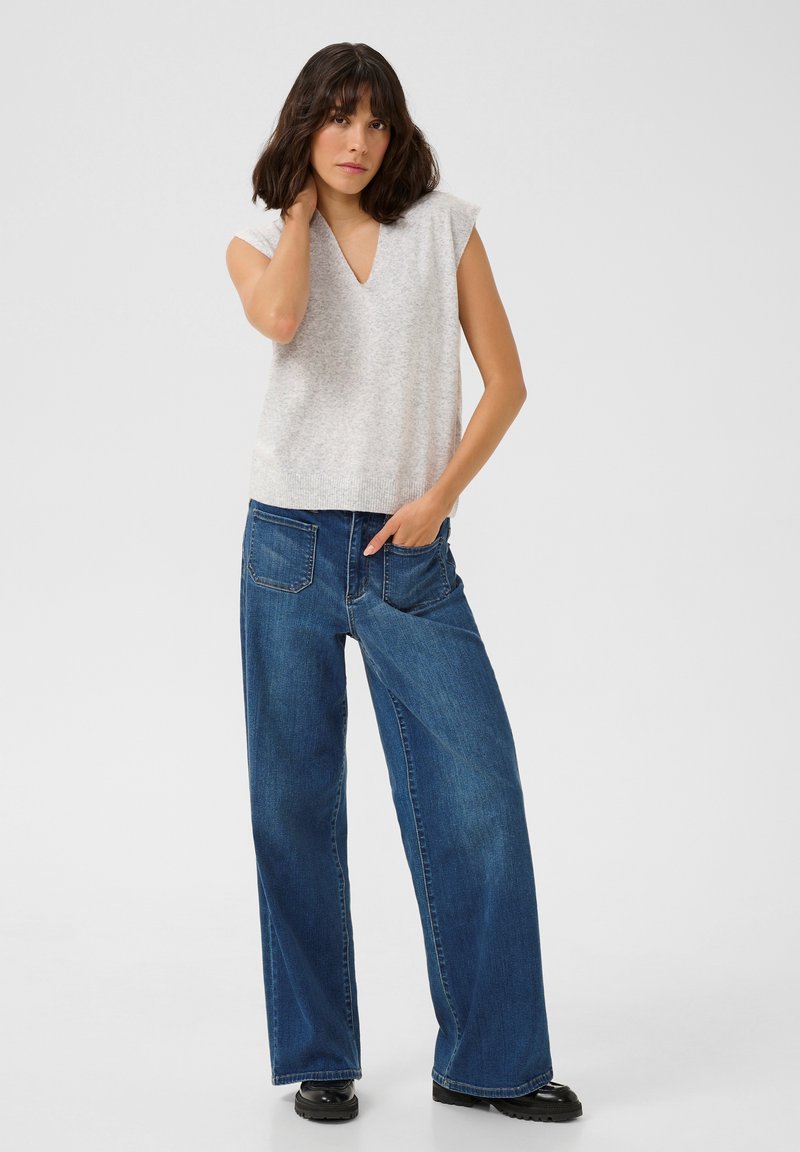 Haut sans manches gris clair avec décolleté en V, associé à un jean en denim bleu à jambes larges. Le haut présente un ourlet côtelé ; le jean a cinq poches.