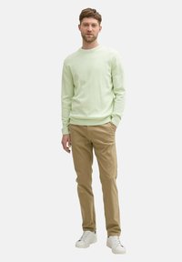 Lichtgroen langarmshirt, kaki broek en witte sneakers. Slanke pasvorm, geribbelde manchetten en een subtiele textuur op het shirt.