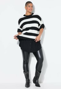 Un pull en tricot à rayures noires et blanches, à manches courtes, superposé sur une chemise noire à boutons. Associé à un legging noir brillant et des bottes cloutées.