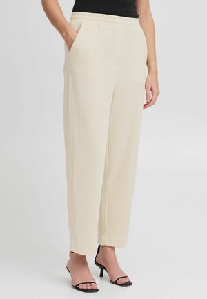 Beige wide-leg pants with a textured surface, featuring an elastic waistband and side pockets. Paired with black strappy heels.