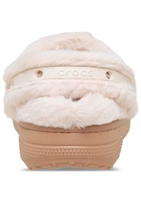 Crocs en fausse fourrure rose avec une semelle en caoutchouc beige et une bande blanche ornée du nom de la marque. Présente des trous de ventilation pour la respirabilité.