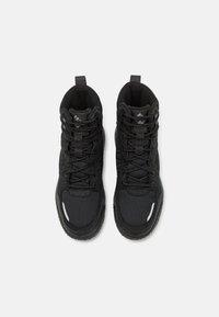Zapatos negros de tobillo con materiales de malla y sintéticos, que presentan una superficie texturizada, punteras redondas y suelas planas con acentos blancos.