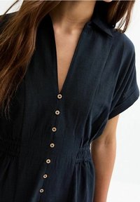Abito camicia con bottoni in un blu navy scuro, caratterizzato da un colletto, maniche corte, vita elastica e dettagli con bottoni in legno.