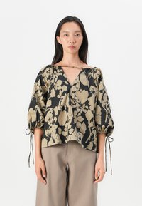 Blouse à imprimé floral noir et beige. Détails d'un col en V, manches ballons avec des accents à cordon, et une coupe loose et cropped.