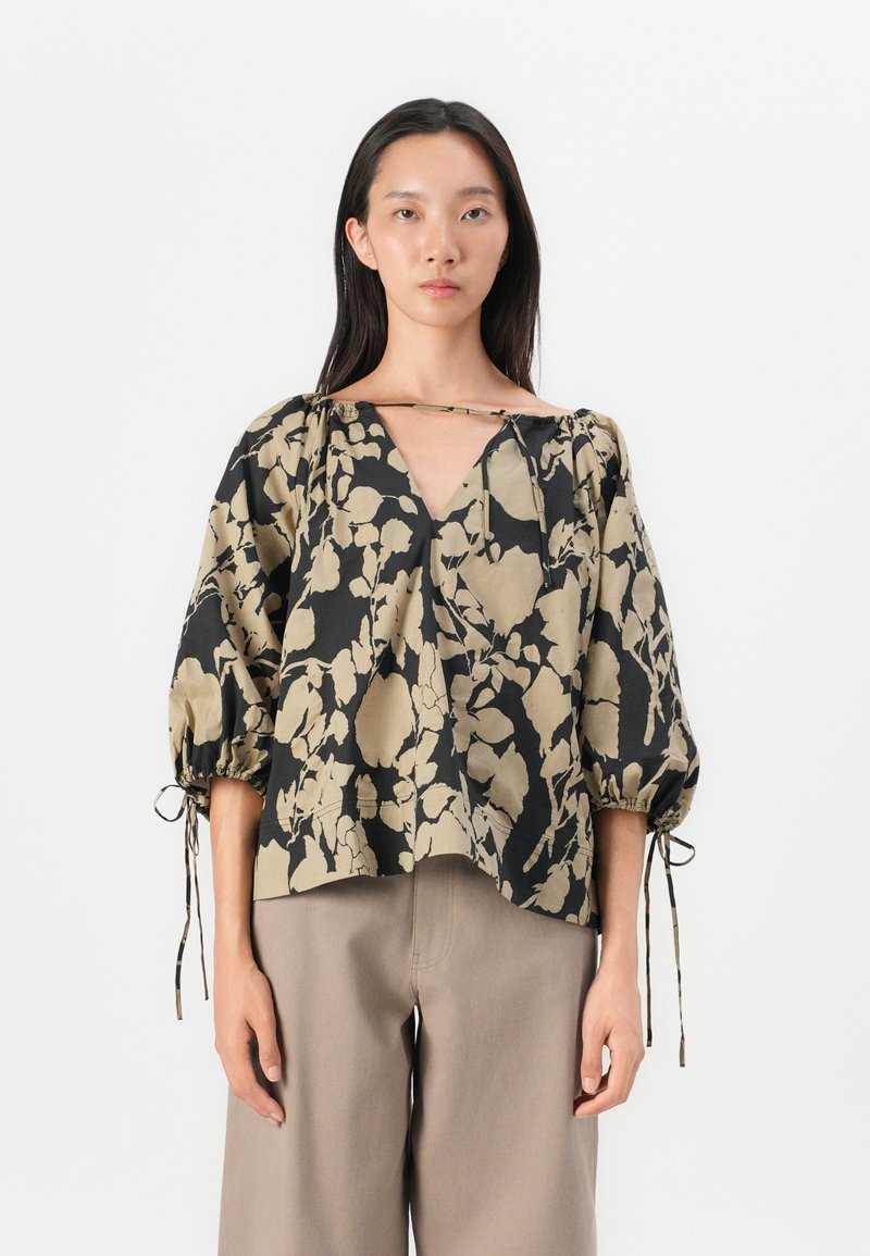 Blouse à imprimé floral noir et beige. Détails d'un col en V, manches ballons avec des accents à cordon, et une coupe loose et cropped.
