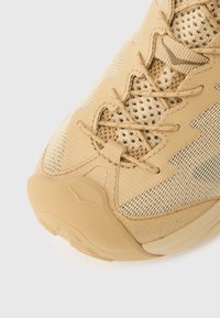 Αθλητικό παπούτσι σε καφέ απόχρωση με υφασμάτινο επάνω μέρος και υφή, ενισχυμένη φτέρνα και καουτσούκ σόλα. Οι κορδόνια περνούν μέσα από ανθεκτικές τρύπες για ασφαλή εφαρμογή.