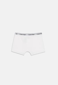 Hvite Calvin Klein boxershorts med svart logo på midjebåndet, mot en enkel lys bakgrunn.