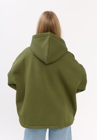 Oversized oliwkowy hoodie z kapturem, wykonany z miękkiego materiału. Design charakteryzuje się opuszczonymi ramionami i zaokrąglonym dołem.