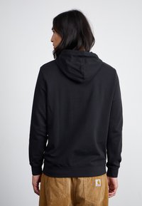 Sort sweatshirt med hætte, lavet af glat materiale; har ribbede manchetter og en søm, båret med strukturerede beige corduroy bukser.