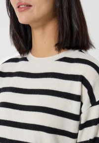 Maglione a righe bianche e nere con scollatura rotonda, realizzato in materiale morbido, caratterizzato da una vestibilità comoda e una texture visibile nel tessuto.