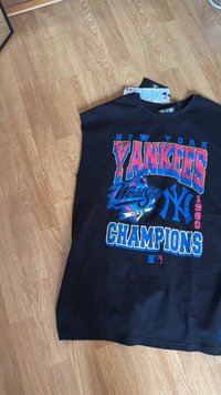 Musta puuvillainen hihaton paita, jossa on rohkeita, värikkäitä grafiikoita: "NEW YORK YANKEES WORLD SERIES CHAMPIONS 1999" joukkueen logolla ja korostuksilla.