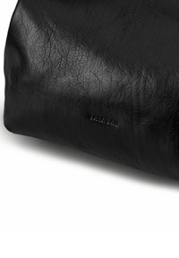 Sac en cuir noir à surface texturée, arborant un logo en relief subtil. La forme est rectangulaire, avec des bords doux et arrondis.