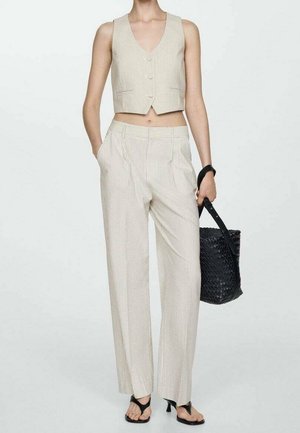Femme portant un gilet sans manches beige à fines rayures et un pantalon taille haute, tenant un sac à main noir tissé, portant des sandales noires à talons.