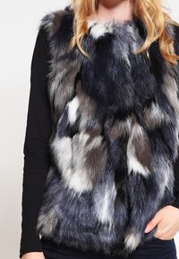 Faux fur-väst med en blandning av mörkgrå, svart och vita mönster, med en mjuk textur och ärmlös design.