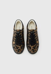 Une paire de baskets noires à lacets ornées de sequins léopard noir et bronze, vues de dessus sur un fond blanc.