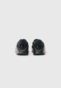 Et par sorte Nike-sneakers set fra bagsiden, som viser teksturerede hæle med store Nike-logoer på en ensfarvet lys baggrund.