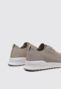 Zapatillas deportivas beige con un upper de malla texturizada y suela flexible, que cuentan con un cuello acolchado y detalles de diseño minimalistas.