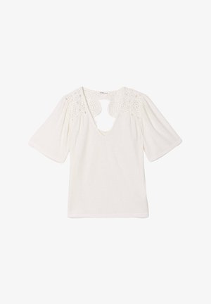 Blouse blanche avec un décolleté en V et des manches courtes bouffantes. Présente des détails en dentelle circulaire sur les épaules et une découpe en forme de clé au dos.