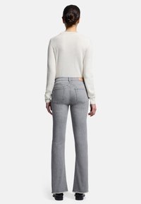 Grå udringede jeans med rå kant, parret med en cremefarvet sweater. Jeansene har høj talje og baglommer, hvilket viser et minimalistisk design.