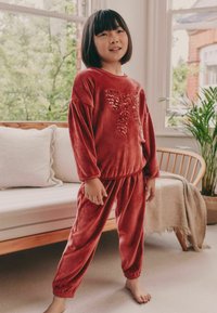 Red velour children’s loungewear set featuring a large sequin bow design on the top. The pants have elastic cuffs at the ankles.