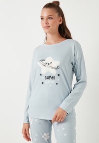 Svijetloplava pidžama koja se sastoji od dugih rukava s plišastim grafičkim uzorkom zvijezde, natpisom "SUPER CUTE" i odgovarajućih hlača s uzorkom zvijezda.