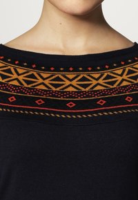 Marineblauer Pullover mit einem bunten geometrischen Muster in Gelb, Rot und Schwarz am Kragen. Weiches Strickmaterial mit weitem Ausschnitt.