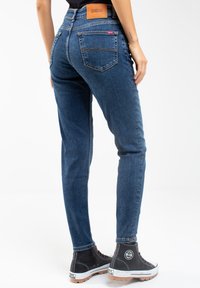 Tummansininen farkkukangas skinny-fit -farkut, joissa on korkea vyötärö, takataskuissa kaarevaa ommelta ja ruskea nahkainen tuotemerkki-patch vyötäröllä.