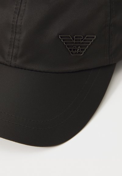 Căciulă neagră dintr-un material fin, cu o margină curbată. Are un logo negru lucios cu un design cu aripi pe partea din față.