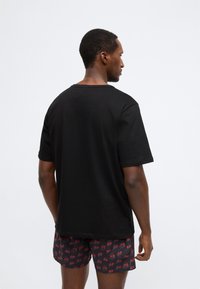 Tricou negru din bumbac cu mâneci scurte și guler rotund, asortat cu pantaloni scurți cu model cu cireșe pe un fundal închis.