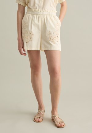 Crème katoenen shorts met een elastische tailleband, met bloemenborduurwerk op de voorkeurs, gecombineerd met beige sandalen met bandjes.