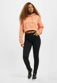 Sudadera corta melocotón con cordones, combinada con jeans ajustados negros. El conjunto presenta una textura suave y un diseño ceñido. Zapatillas negras.