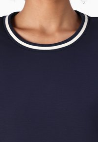 Mørkeblå t-skjorte med rund hals og en kontrasterende hvit stripe. Stoffet fremstår glatt og lett.