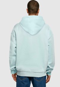 Felpa blu chiaro con un ampio cappuccio e spalle cadenti, realizzata in un tessuto morbido; presenta polsi e orlo a coste. Indossata sopra jeans in denim.