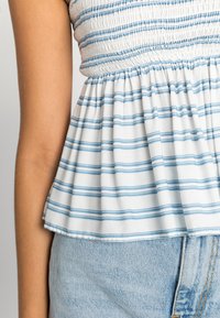 Top peplum às riscas azul e branca com corpete franzido, apresentando tecido de algodão suave e uma bainha ampla. Combinado com calções de ganga.