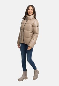 Beige puffjacka med hög krage, frontdragkedja och kviltat mönster. Kombinerad med blå jeans och beiga ankelstövlar.