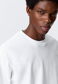 Hvid crewneck t-shirt lavet af bomuld med korte ærmer, der har en afslappet pasform og en glat tekstur. Udhæftningen er ribbet.