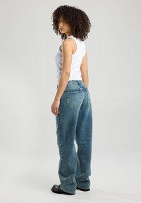 Lichtblauwe hoge taille jeans met een relaxte pasvorm, voorzien van achterzakken en een vervaagde textuur, gecombineerd met een witte fitted tanktop.