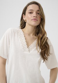 T-shirt beige à manches courtes avec un col en dentelle festonnée ; tissu doux et coupe décontractée.