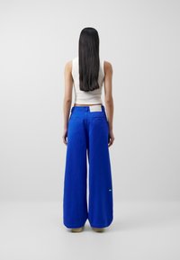 Breda blå byxor i en mjuk väv med en enkel midjeband, bakfickor och en liten grön detalj.