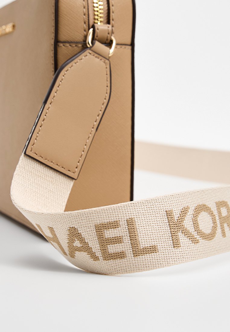 Sac bandoulière beige à finition texturée, fermeture éclair dorée et sangle en tissu ornée du logo "MICHAEL KORS" en lettres dorées.