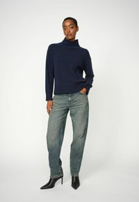 Marineblauwe coltrui met ribbelstructuur, gecombineerd met losse lichtblauwe jeans en zwarte puntige hakken. Eenvoudige, gestructureerde stof.