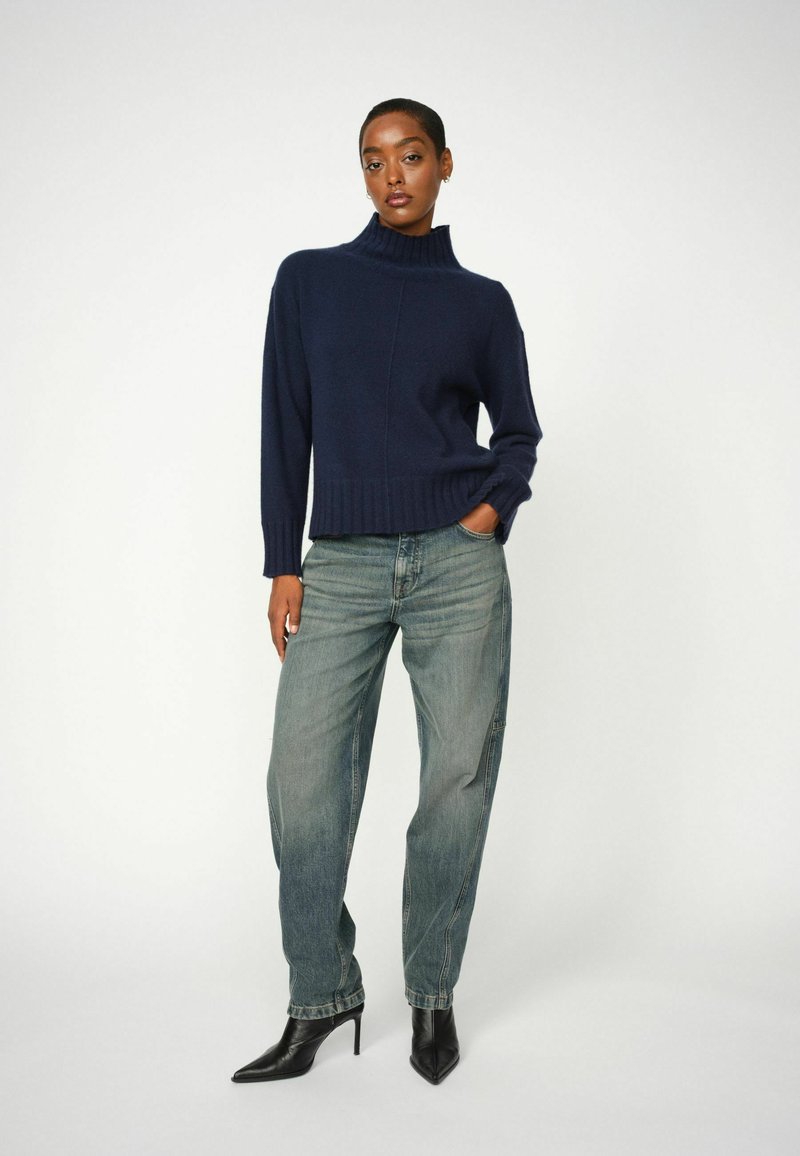 Marineblauwe coltrui met ribbelstructuur, gecombineerd met losse lichtblauwe jeans en zwarte puntige hakken. Eenvoudige, gestructureerde stof.