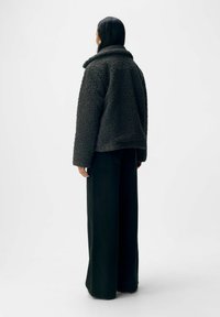 Veste en peluche grise foncée avec un large col ; présente une coupe carrée et est associée à un pantalon large noir taille haute.