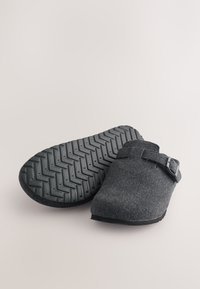 Sabots en feutre gris avec une semelle en caoutchouc texturée, dotés d'une lanière et d'un design à dos ouvert pour un enfilage facile.